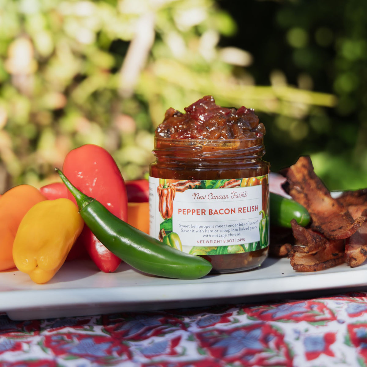 Jar of Pepper Bacon Relish with peppers and bacon on a tray outdoors