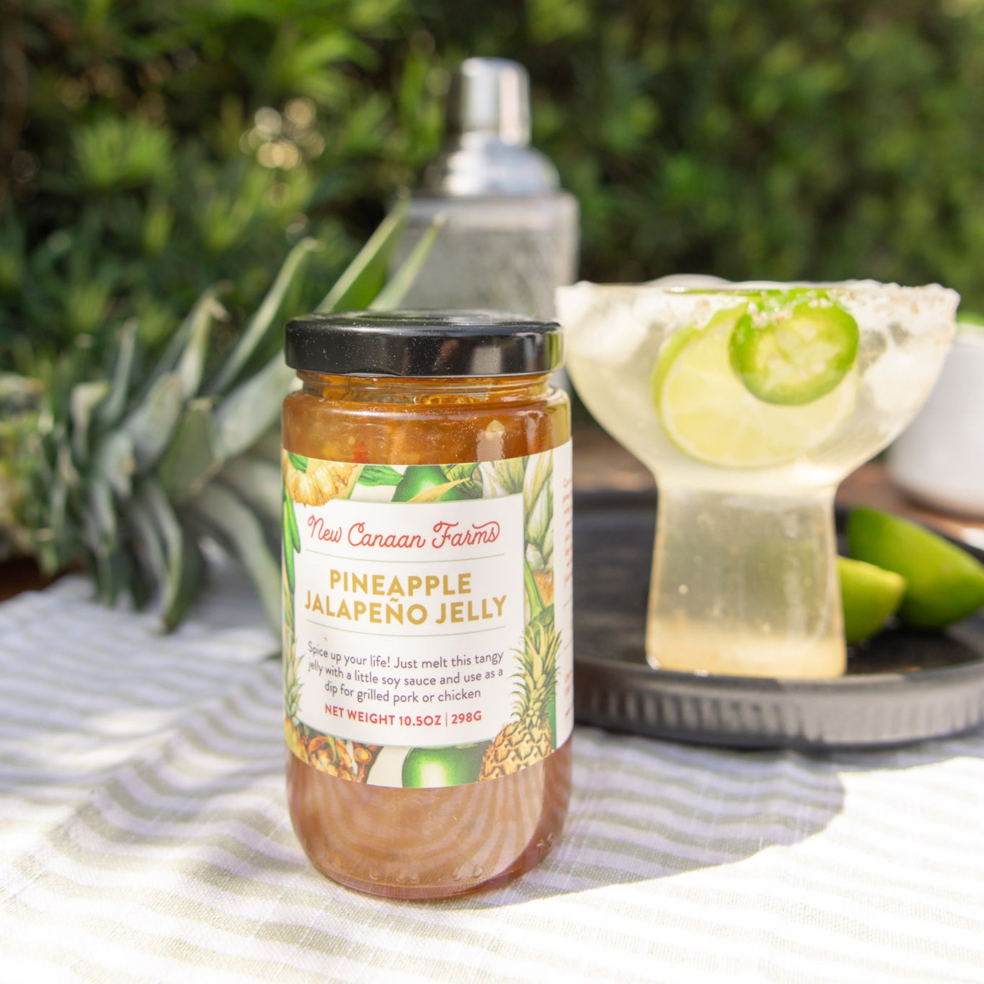 Jar of Pineapple Jalapeno Jelly on a table with a cocktail in the background