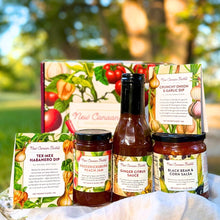 A curated collection of five New Canaan Farms  jams, sauces, salsas and spice blends, in front of a vegetable-designed gift box, photographed outside