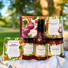 A curated collection of five New Canaan Farms  jams, sauces, salsas and spice blends, in front of a seasonally-inspired gift box, outside