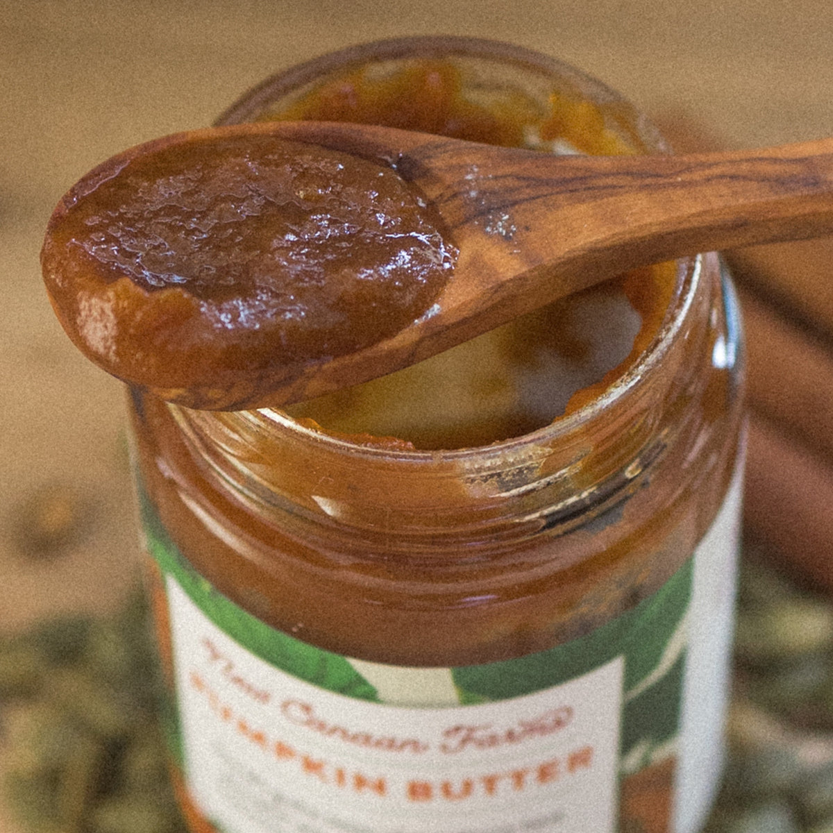 Close-up of a wooden spoon of Pumpkin Butter over an open jar of New Canaan Farms Pumpkin Butter