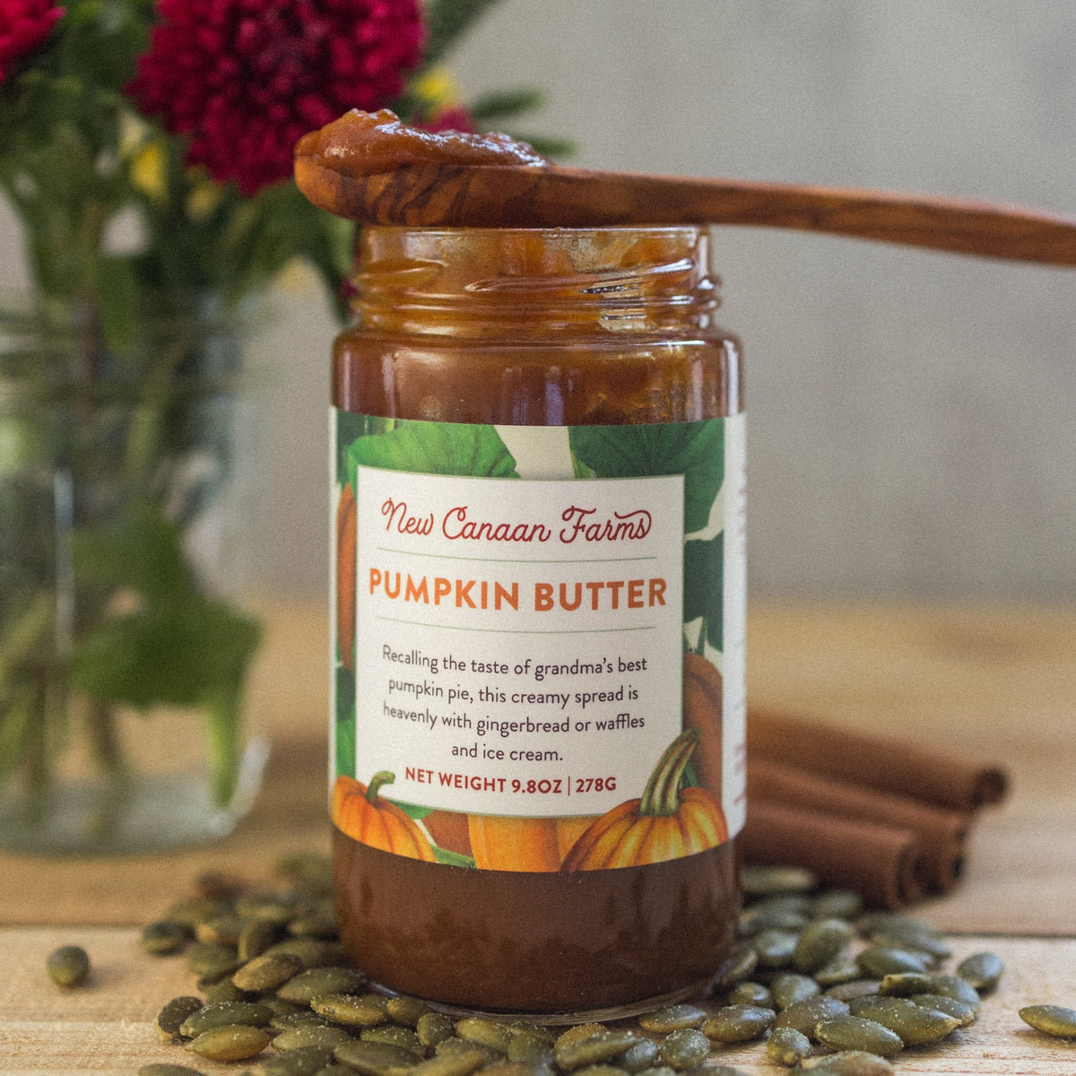 New Canaan Farms Pumpkin Butter jar with a spoonful on top, surrounded by pumpkin seeds