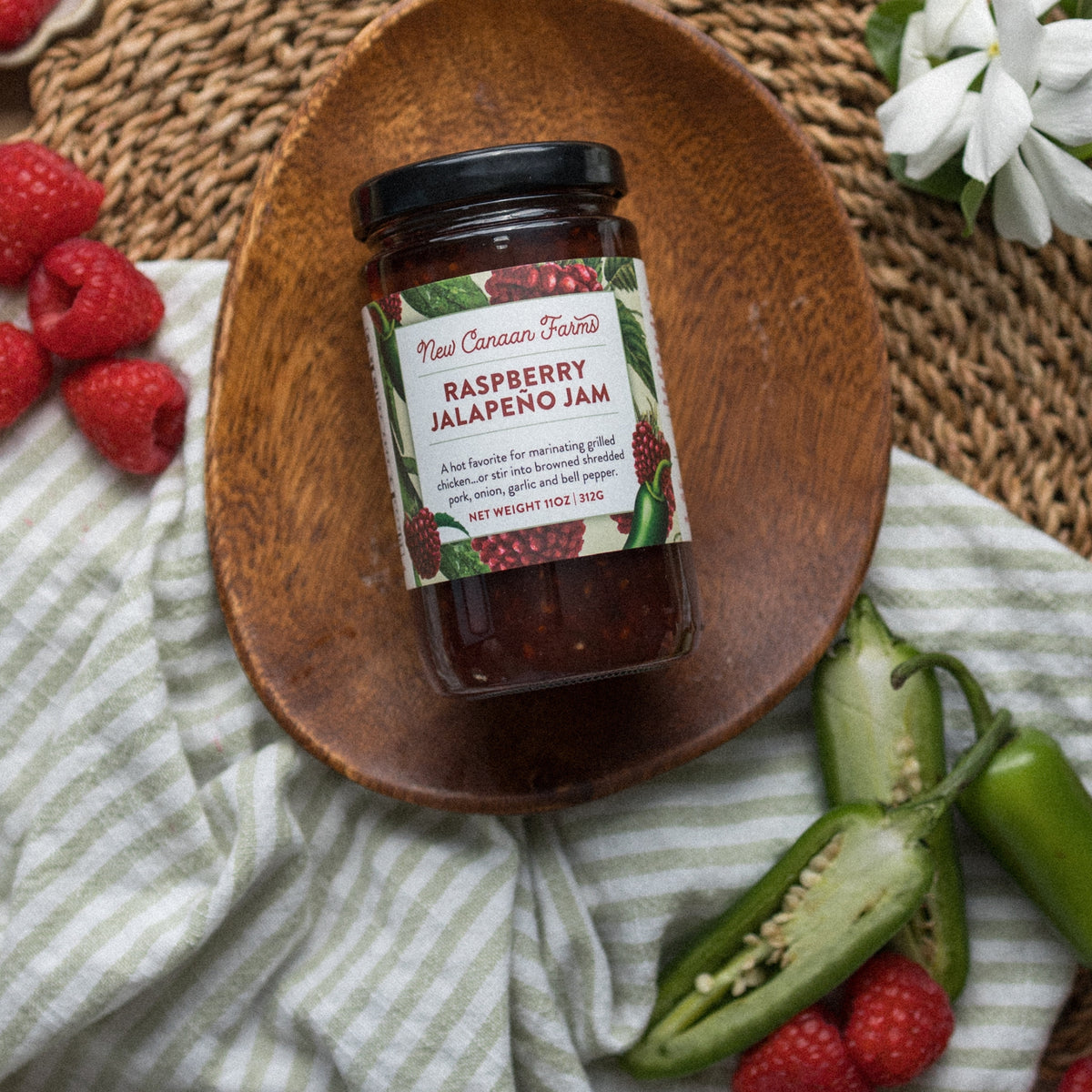 New Canaan Farms Raspberry Jalapeño Jam jar in a wooden dish with raspberries and jalapeños