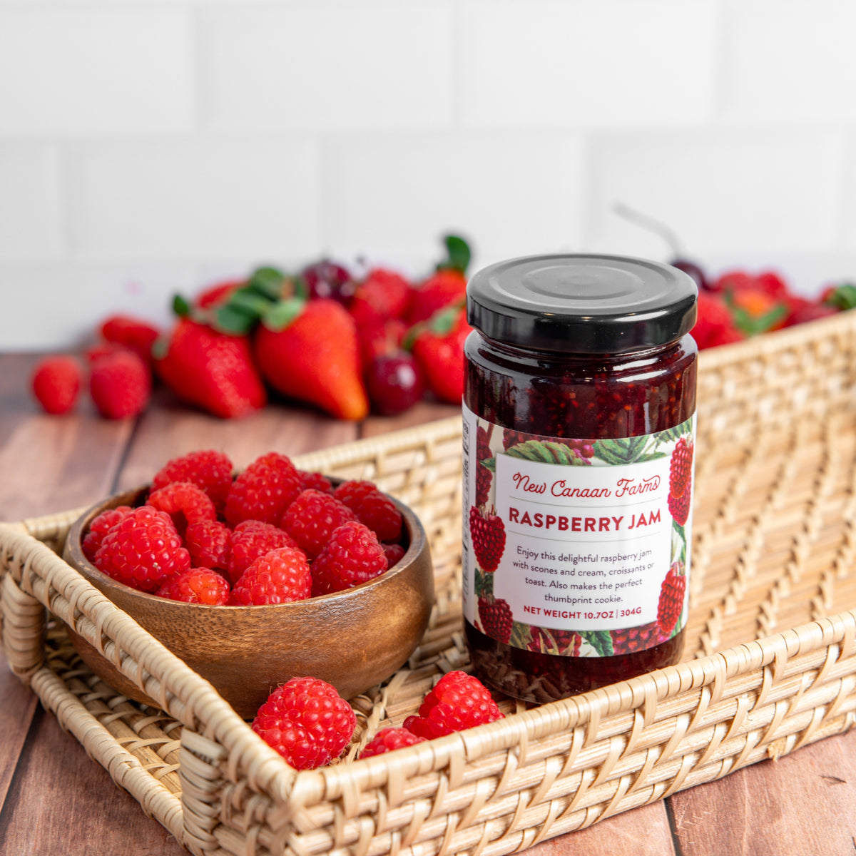 Jar of raspberry jam with a bowl of raspberries and strawberries on a wooden tray.