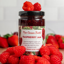 Jar of New Canaan Farms Raspberry Jam surrounded by fresh raspberries on a light background