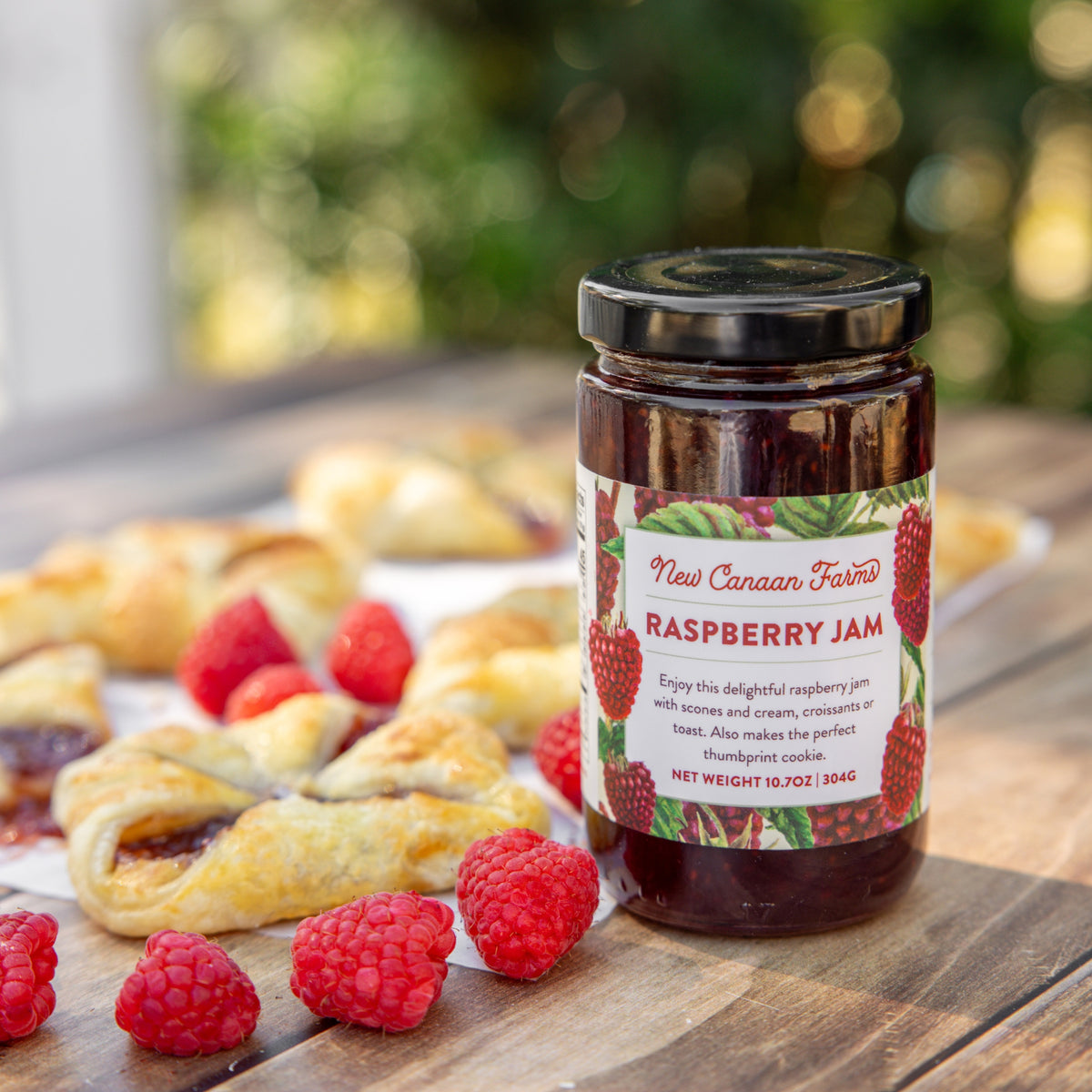 Jar of New Canaan Farms Raspberry Jam with pastries and raspberries on a wooden surface