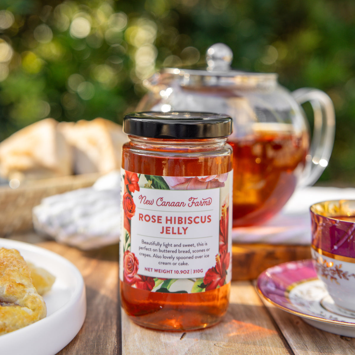 Jar of New Canaan Farms Rose Hibiscus Jelly on a table with tea and pastries