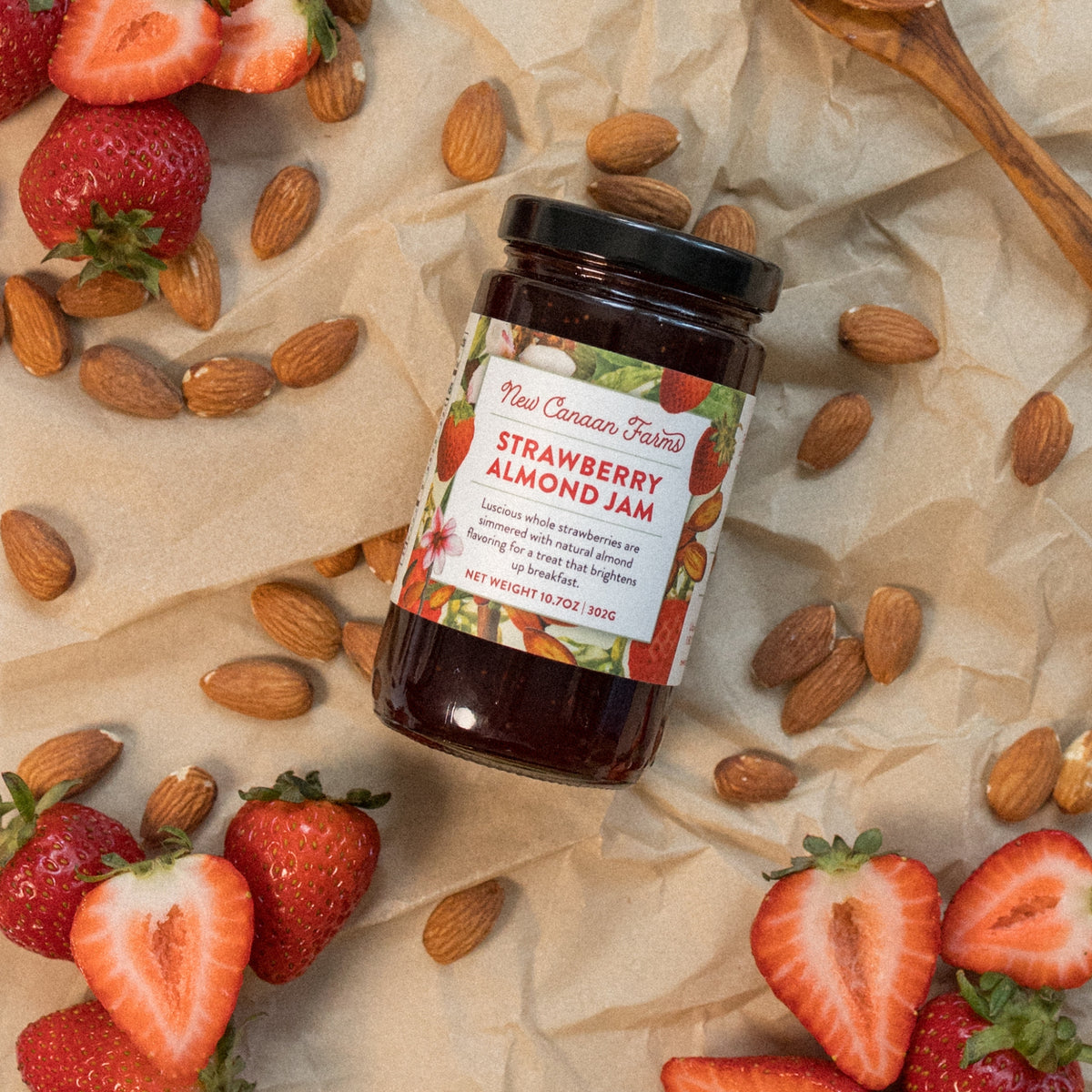 New Canaan Farms Strawberry Almond Jam jar lying among almonds and strawberries on parchment paper