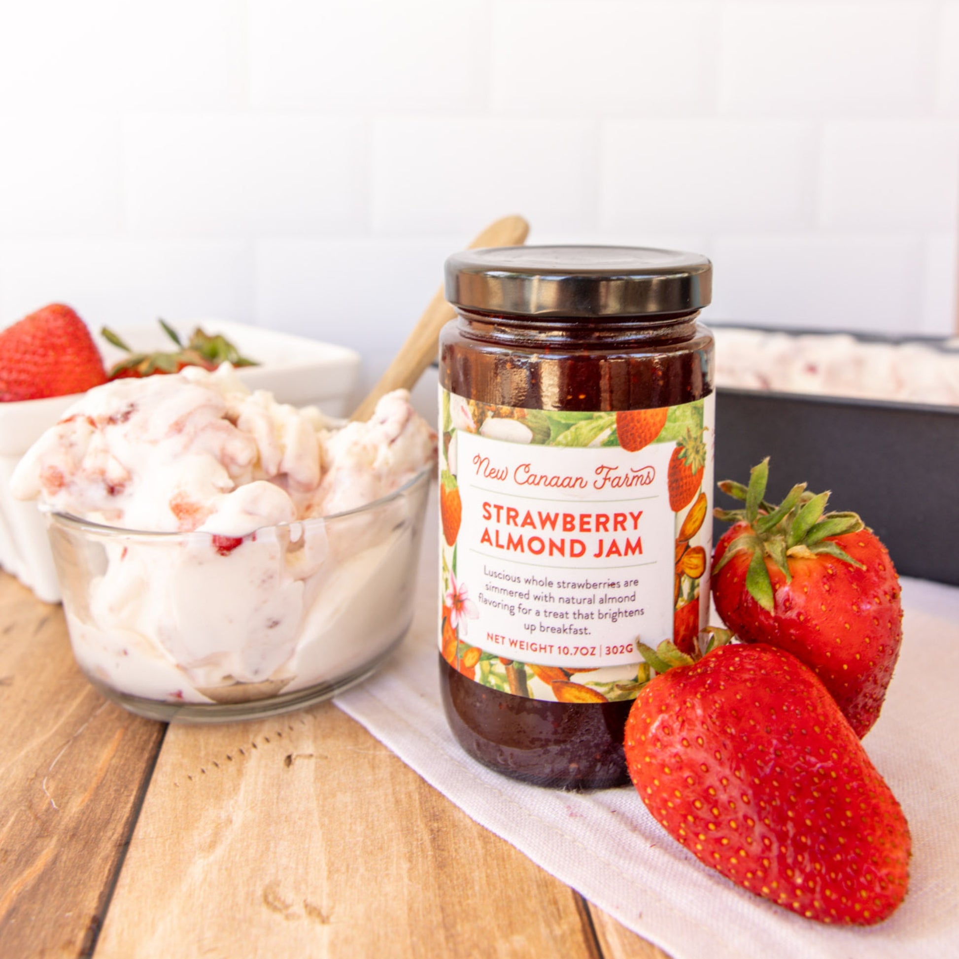 Jar of New Canaan Farms Strawberry Almond Jam with strawberries on a wooden table