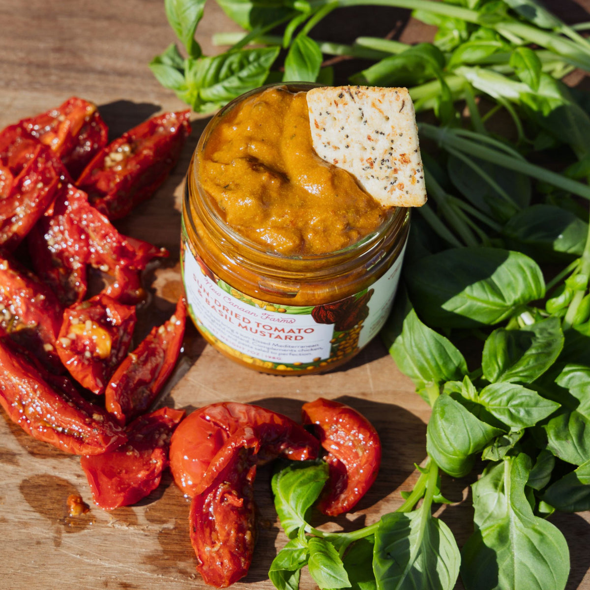 Jar of roasted tomato mustard with dried tomatoes and basil on a wooden board