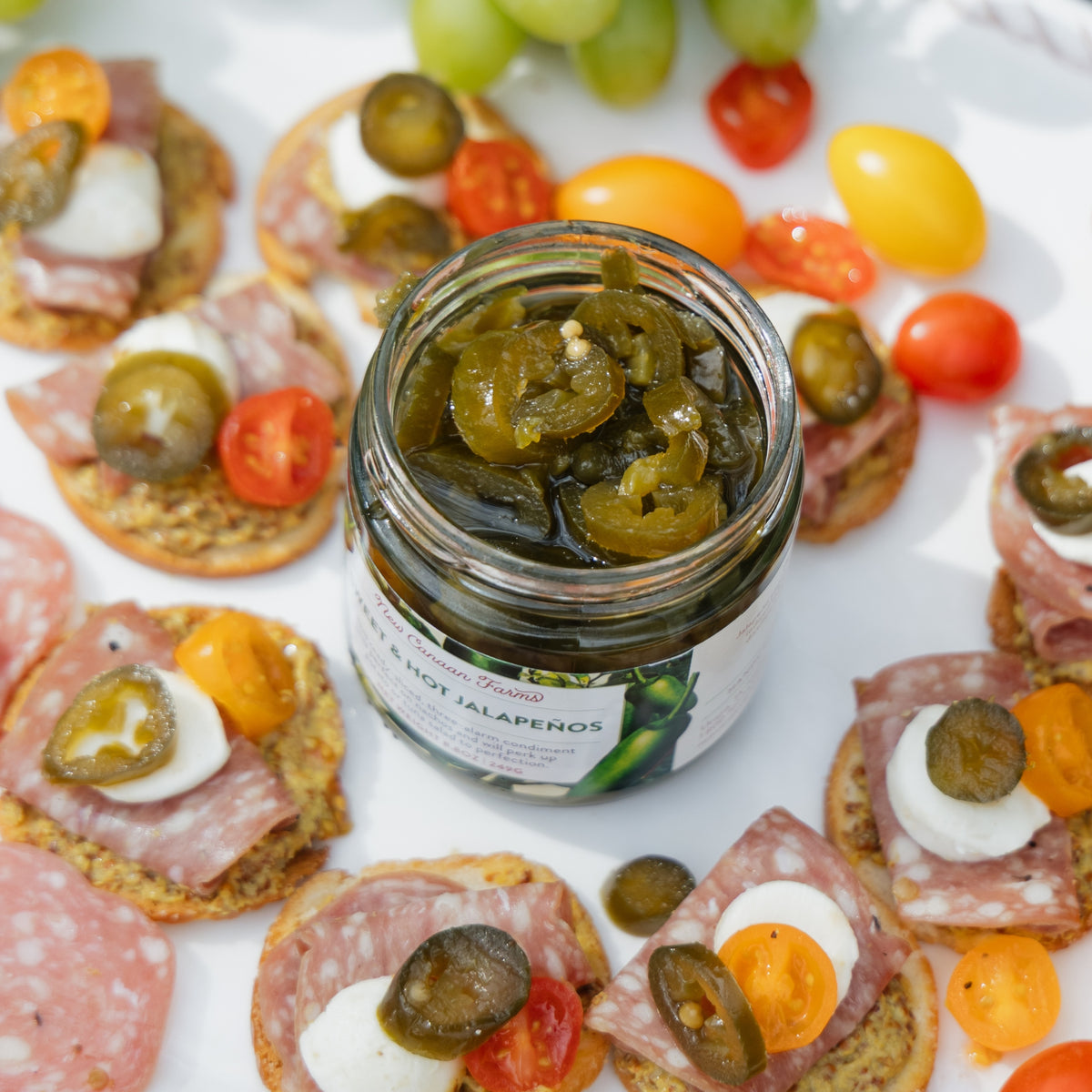 Jar of New Canaan Farms sweet & hot jalapeños on a platter with assorted meats and vegetables