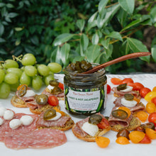 Platter of appetizers with a jar of New Canaan Farms sweet and hot jalapeños on a table outdoors.