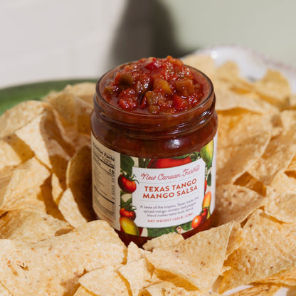 Jar of Texas Tango Mango Salsa surrounded by tortilla chips on a plate.