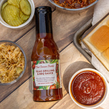 Bottle of Tejas Grilling & BBQ Sauce on a wooden table with sides and bread.