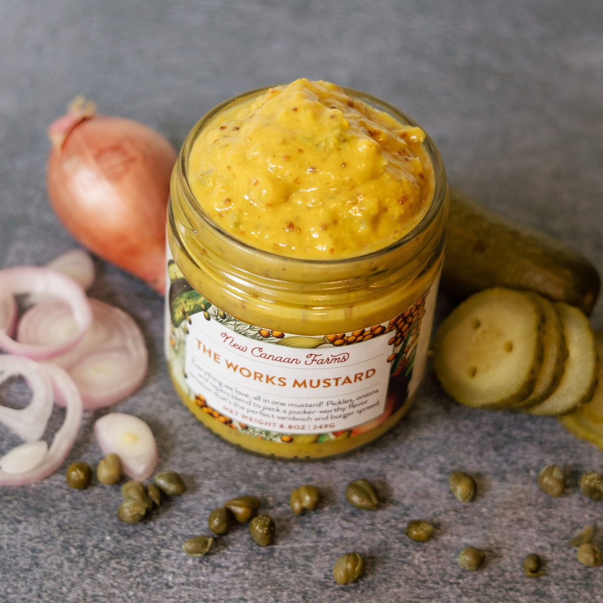 Jar of New Canaan Farms mustard with ingredients like onions and pickles on a gray background