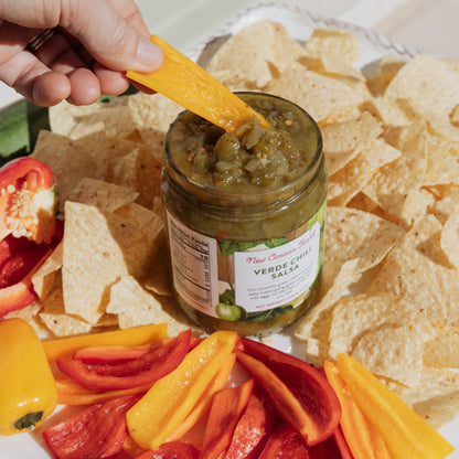 Jar of verde chile salsa with tortilla chips and sliced peppers on a plate