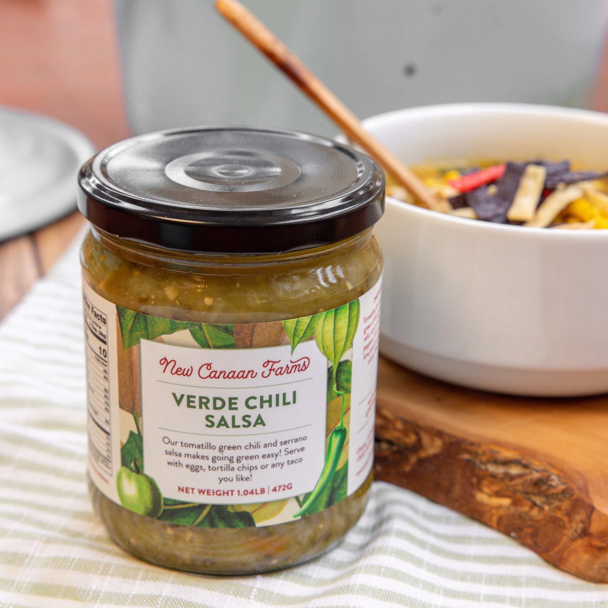 Jar of New Canaan Farms Verde Chili Salsa on a table with a bowl of salad in the background