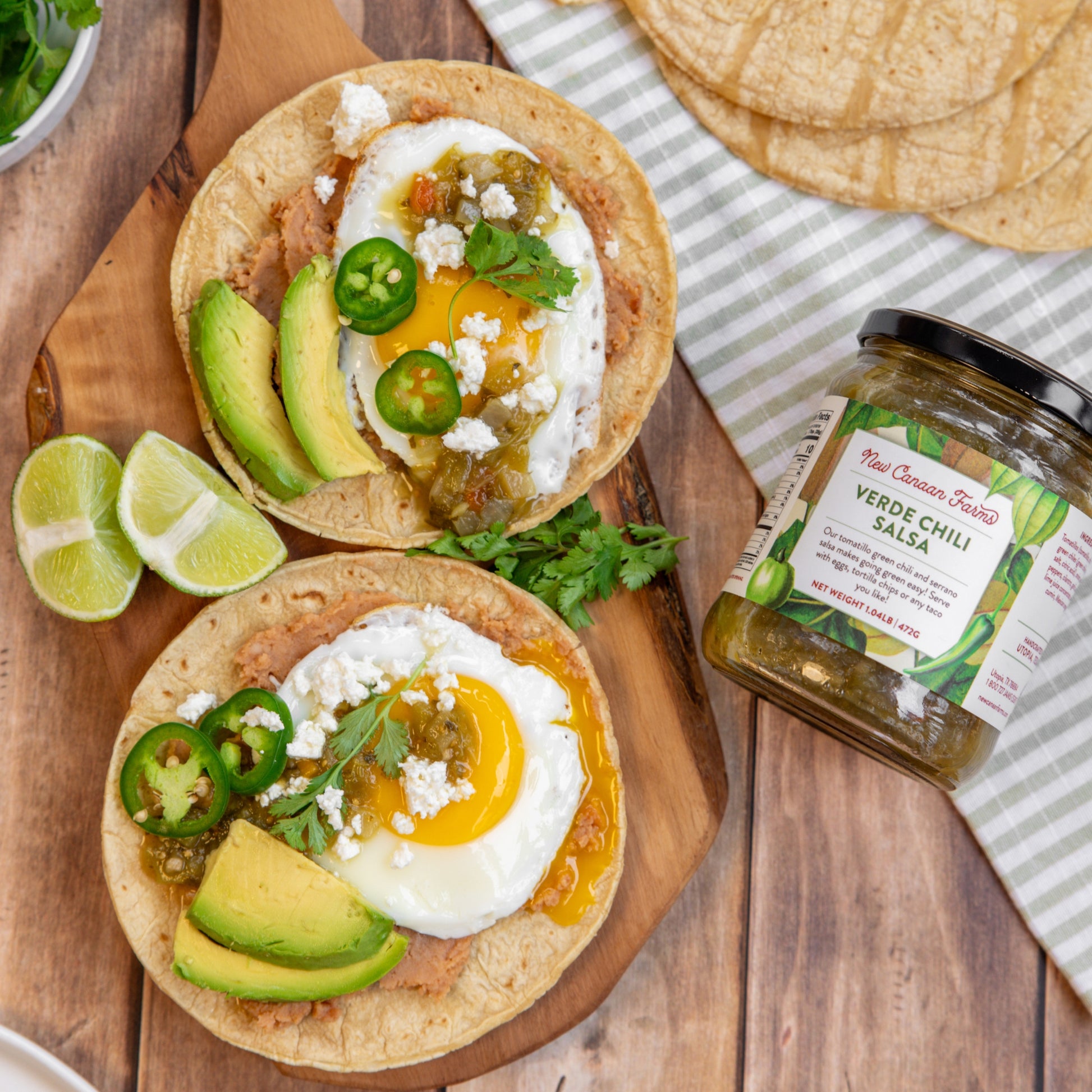 Two tortillas with eggs, avocado, and jalapeños on a wooden board with a jar of salsa.