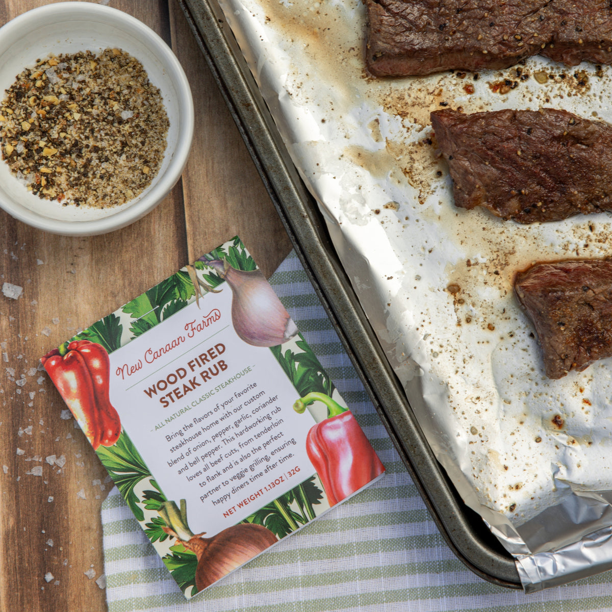 Wood fired steak rub packet next to cooked steaks on a baking tray.