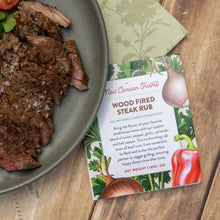 Wood fired steak rub package next to a plate of sliced steak on a wooden surface