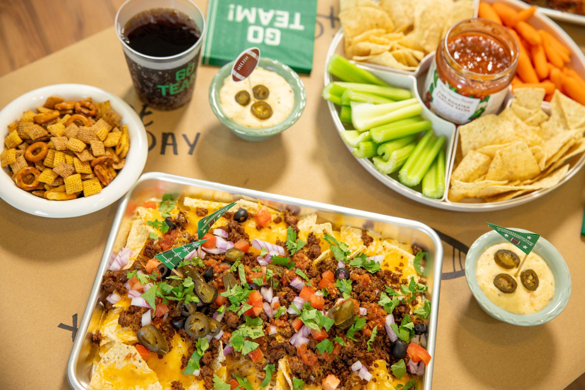 Game day spread with sheet pan nachos, chips, salsa and dips on a table