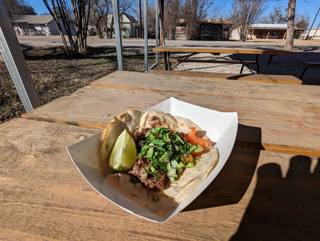 Tortilla with meat, vegetables, and a lime wedge on a wooden table outdoors.