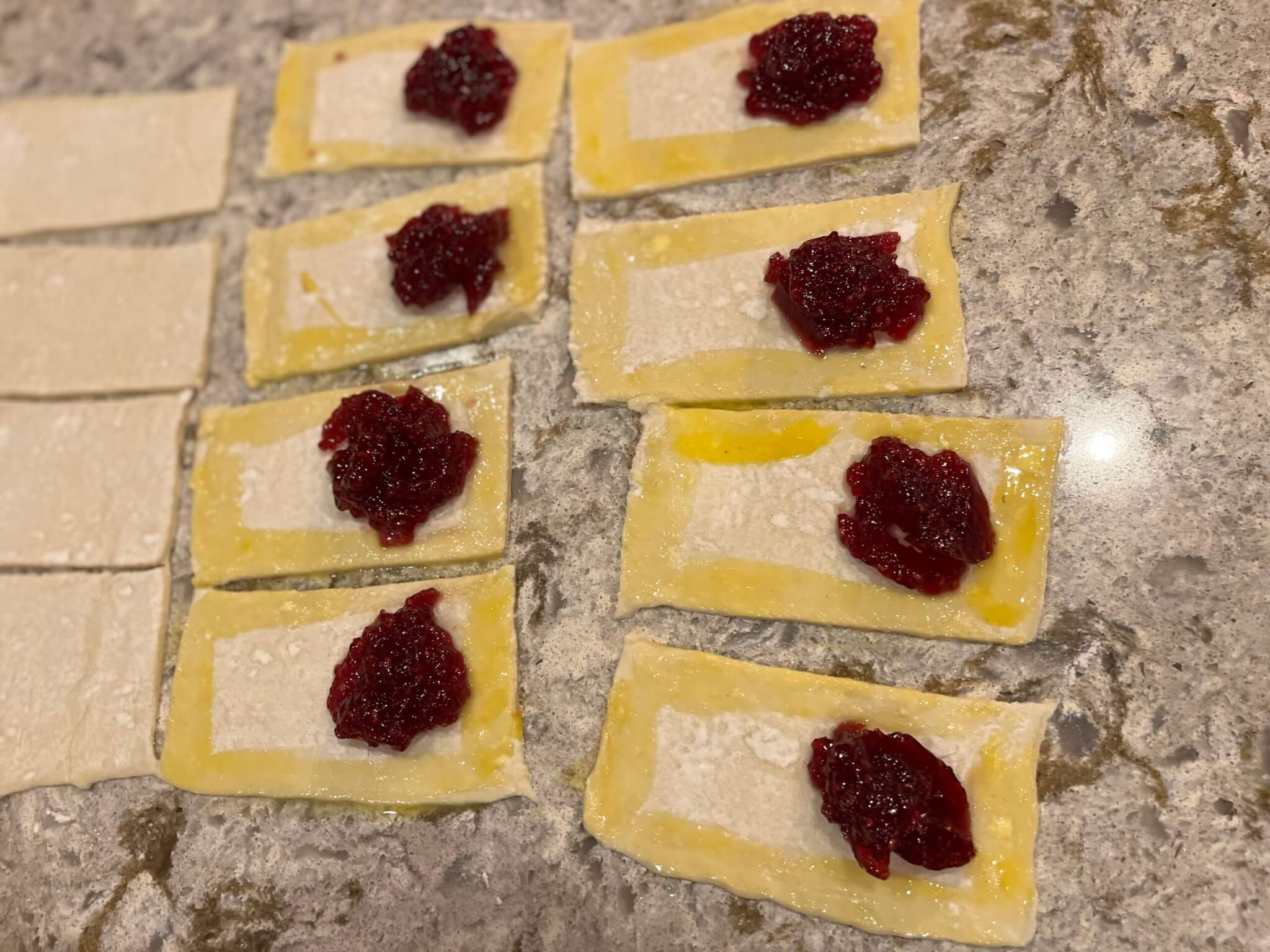 Teaspoons of New Canaan Farms Raspberry Jam  placed on rectangles of puff pastry, with beaten egg around the sides