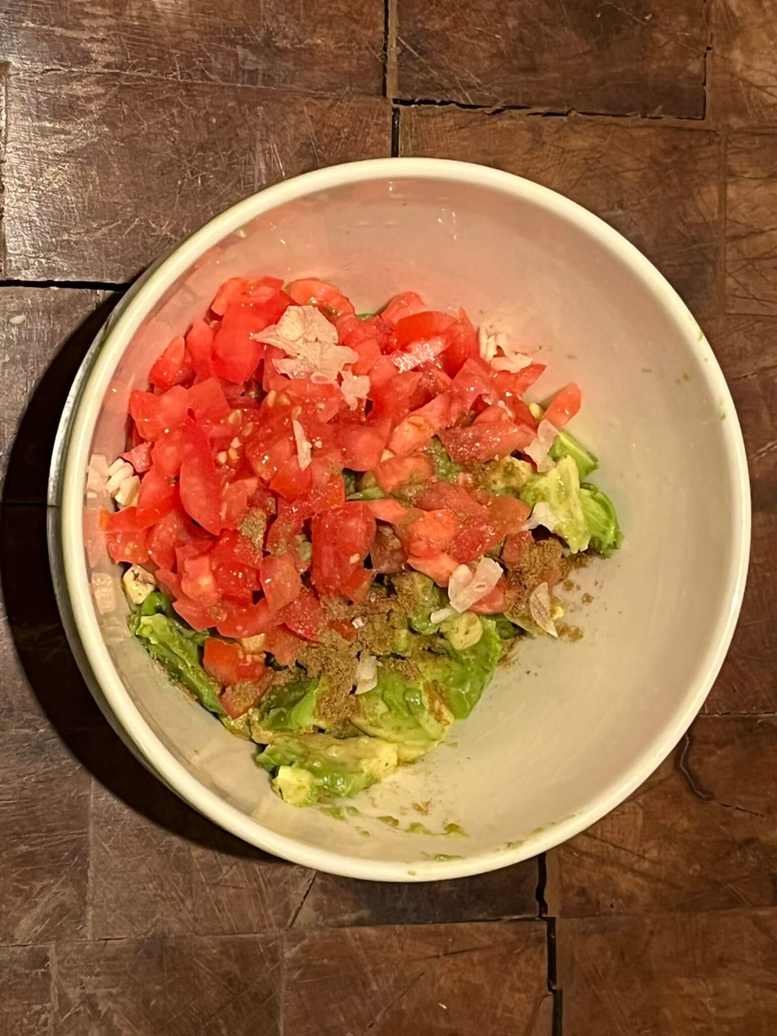 Diced tomatoes and chopped avocados mixed together with spices in a bowl