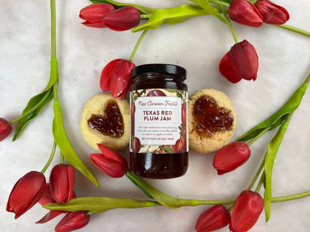 A jar of New Canaan Farms Red Plum Jam, surrounded by Valentine Jam cookies and red tulips