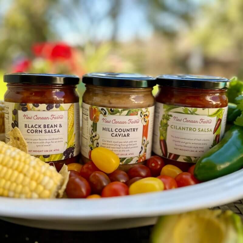 Three chunky New Canaan Farms salsas - Black Bean & Corn, Hill Country Caviar and Cilantro - in a white bowl with fresh vegetables