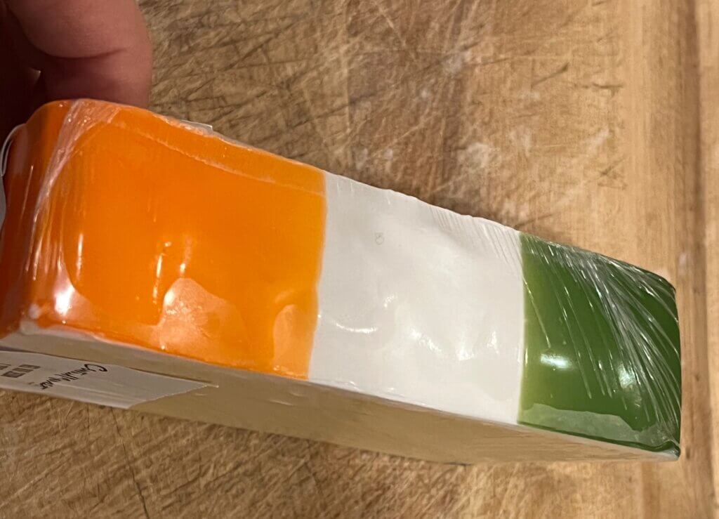 A chunk of Irish cheddar cheese with the Irish flag colors on the rind