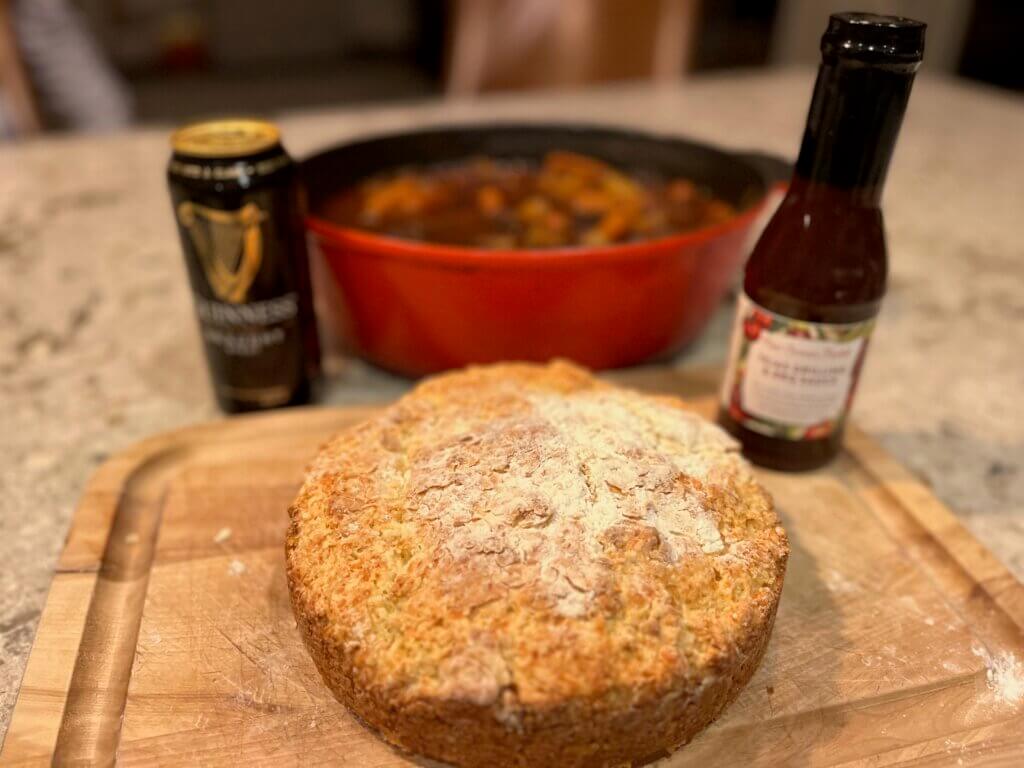 A freshly cooked loaf of Irish cheese soda bread, in from of a pan of Irish stew