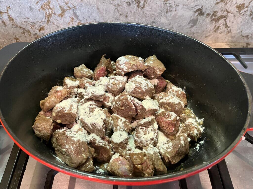 A casserole full of browned meat, with flour sprinkled on top