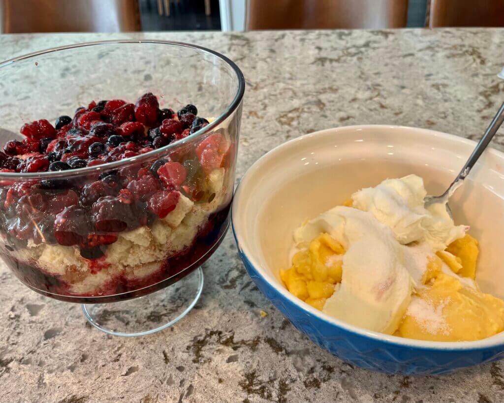 One large glass serving dish with mixed berries and cake inside, next to a bowl of custard and marscapone. Ingredients to build a trifle!