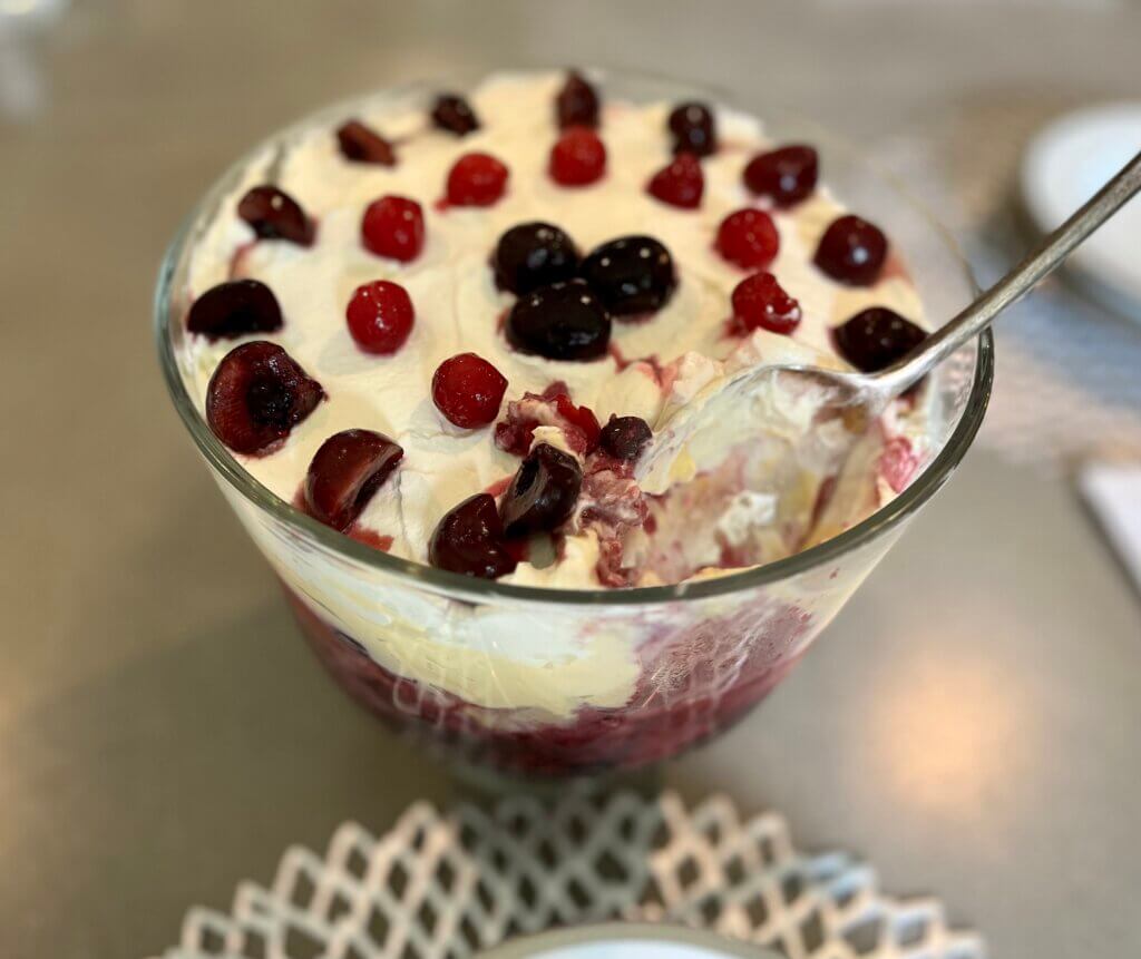 A large glass bowl filled with Trifle, garnished with raspberries and cherries
