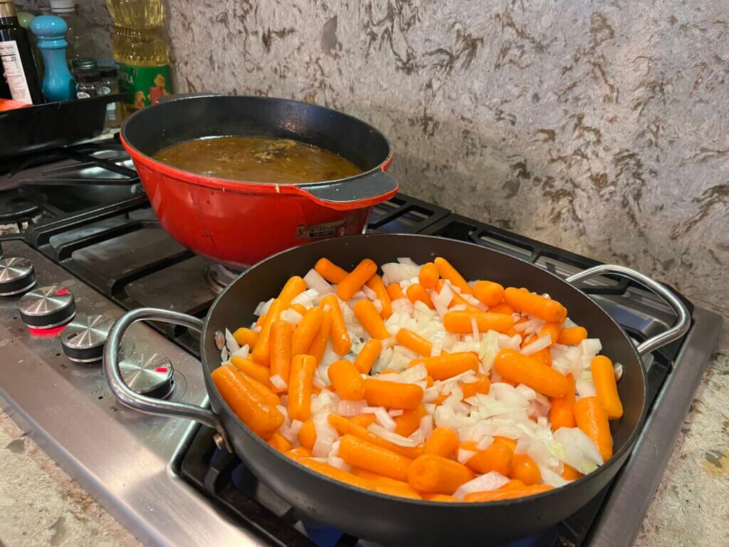Carrots and onion sautéing in a pan, in front of a pan of Irish Stew