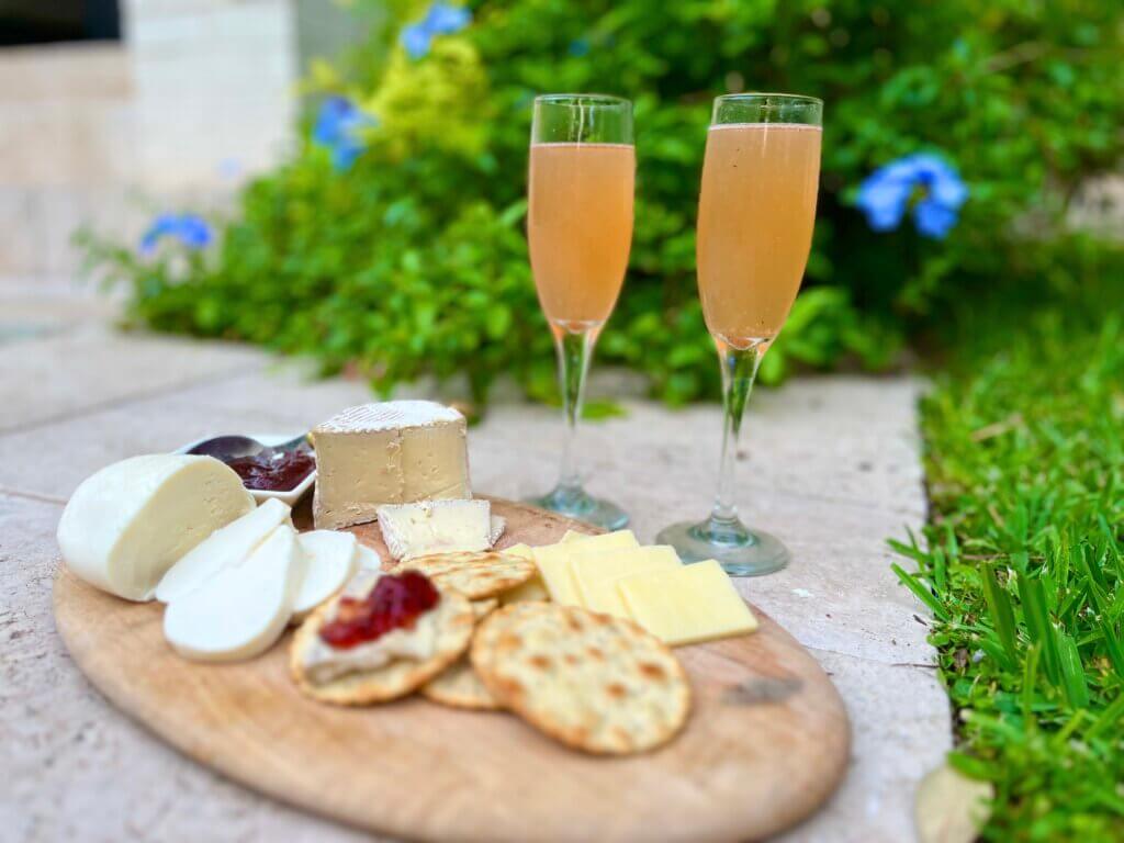 Two champagne glasses containing a plum jam summer cocktail next to a cheese platter