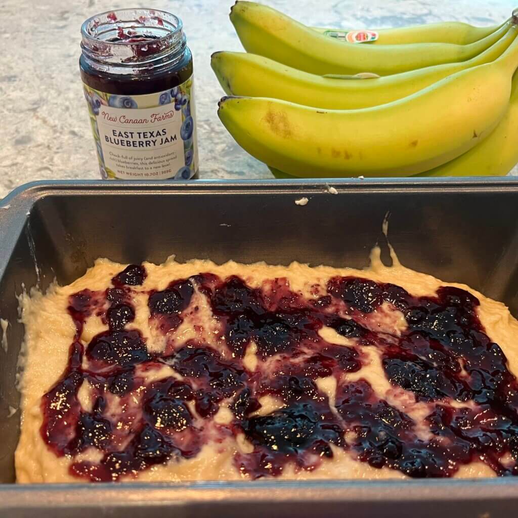 Banana bread batter in a pan, spread with New Canaan Farms blueberry jam
