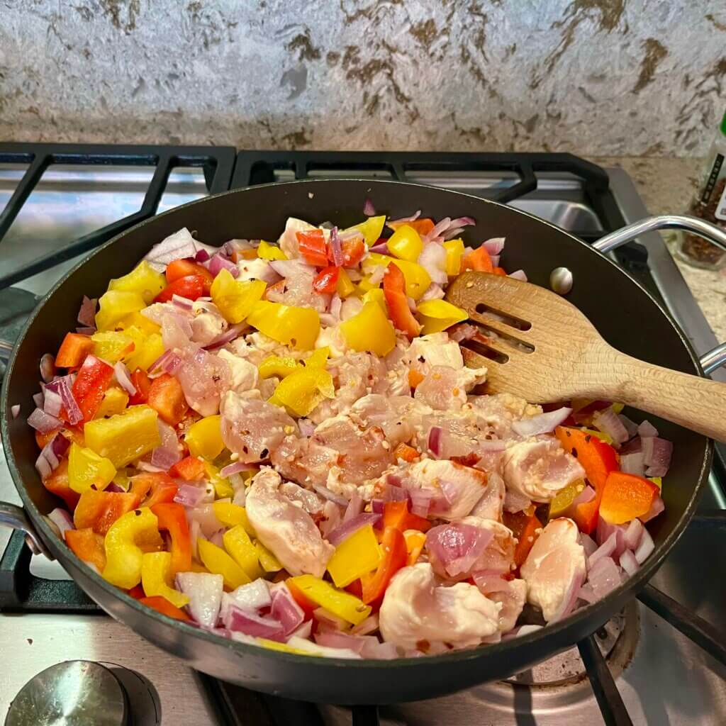 Chicken cooking with peppers and onions in a deep frying pan on the stove
