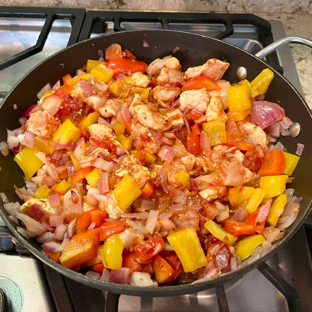 Chicken pieces, peppers, onions and red pepper flakes cooking on the stovetop
