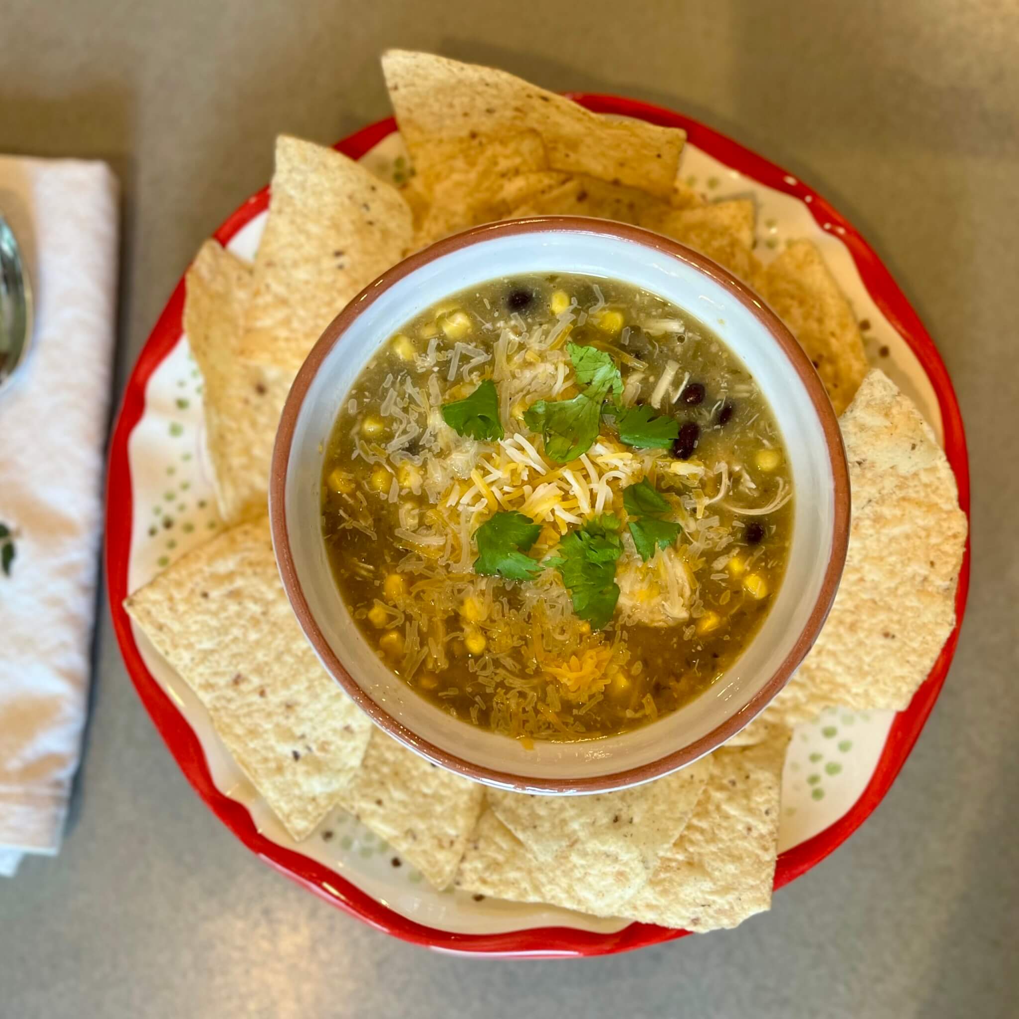 A bowl of chicken tortilla soup, surrounded by tortilla chips