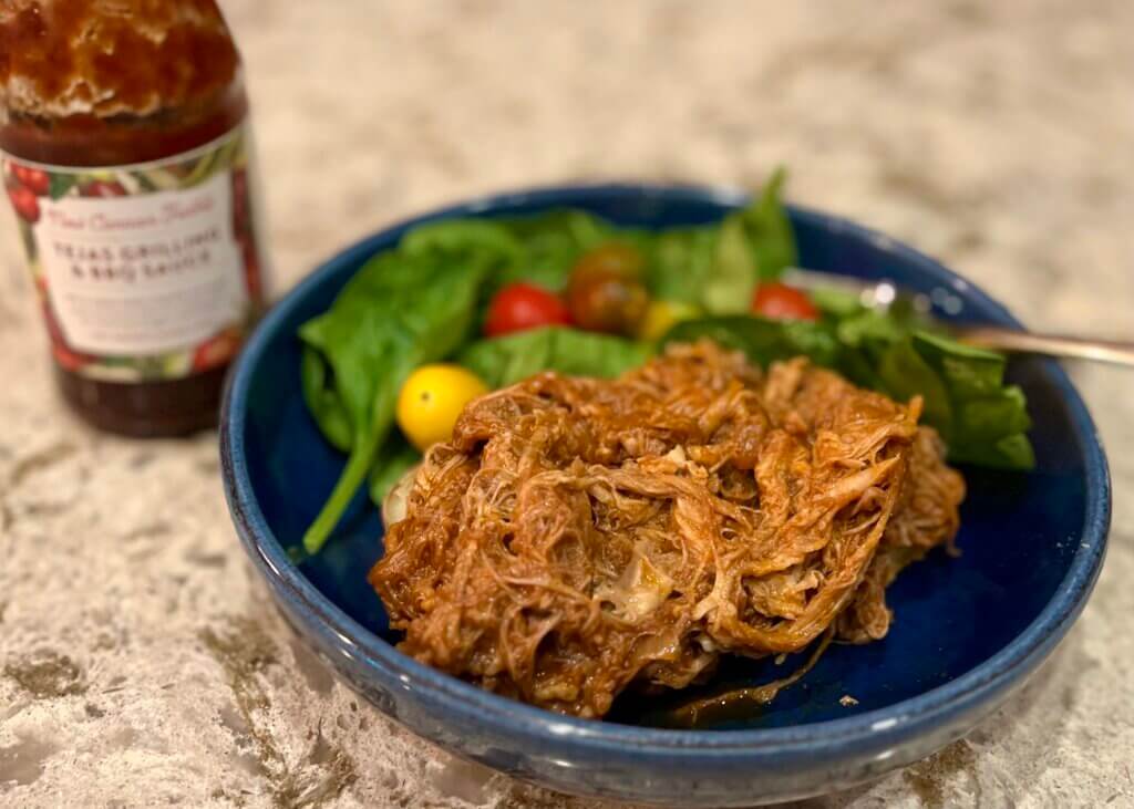 Pulled Pork, made with New Canaan Farms Texas BBQ sauce, served on a baked potato on a blue plate, with a side salad