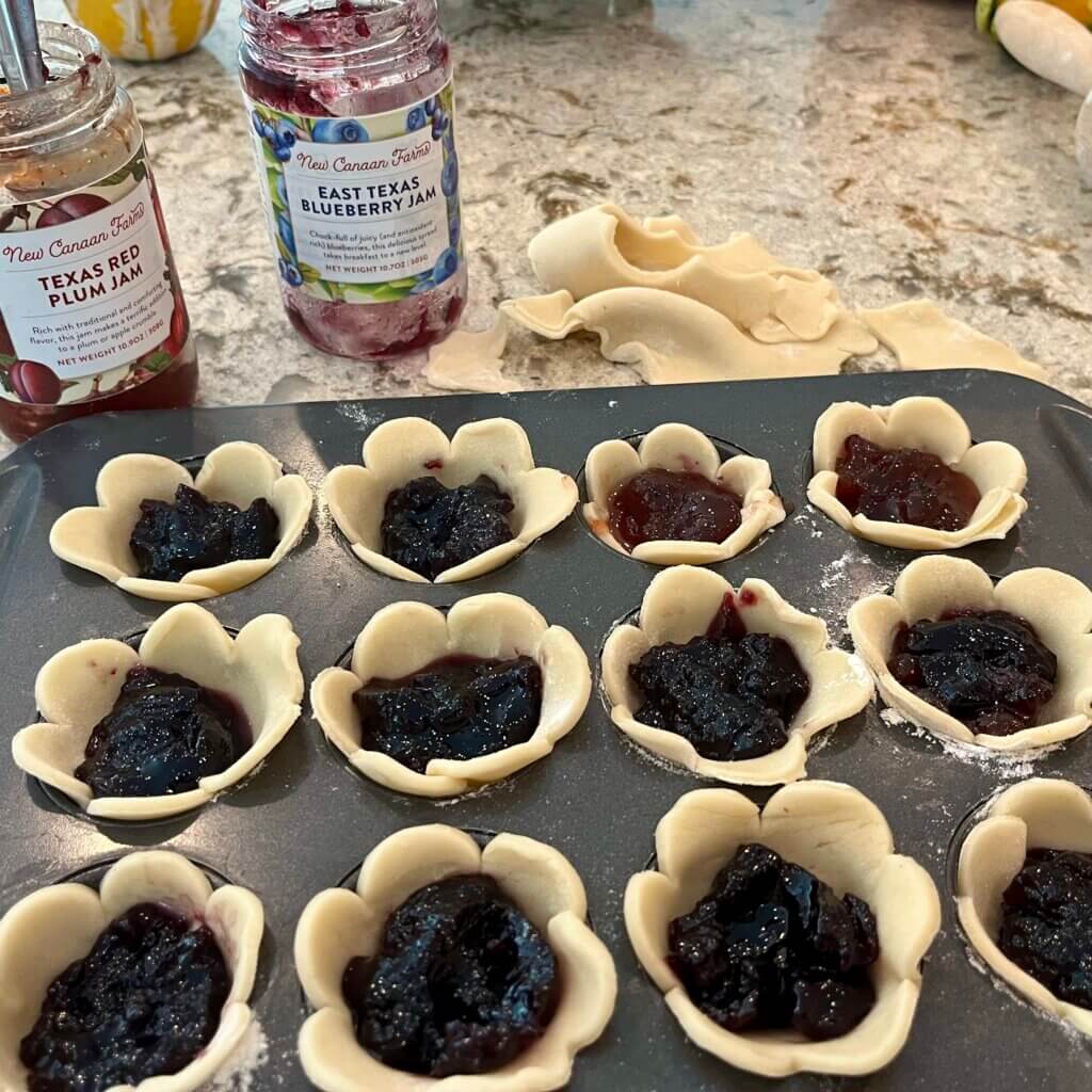 Uncooked pastry filled with New Canaan Farms Blueberry Jam in a muffin pan, about to go into the oven
