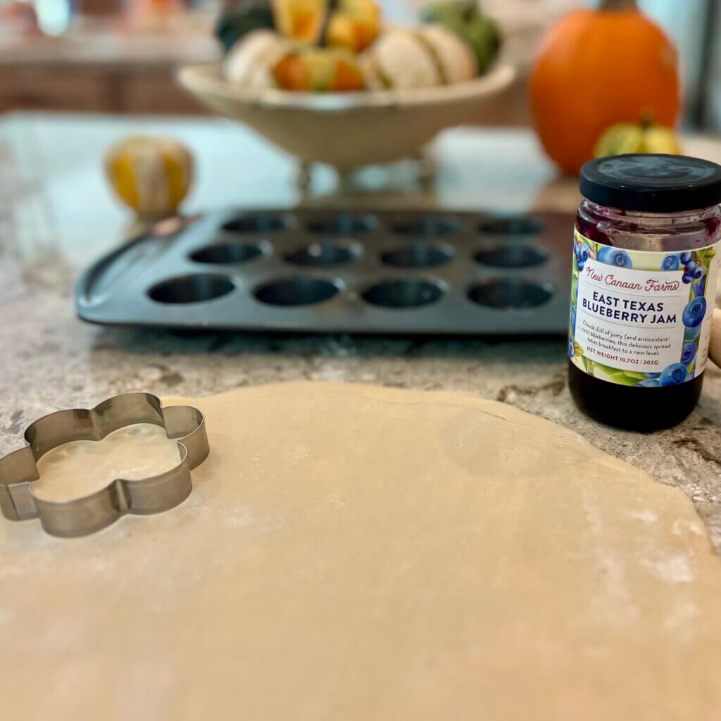 Rolled out shortcrust pastry, with a flower-shaped cutter and a jar of New Canaan Farms Blueberry Jam
