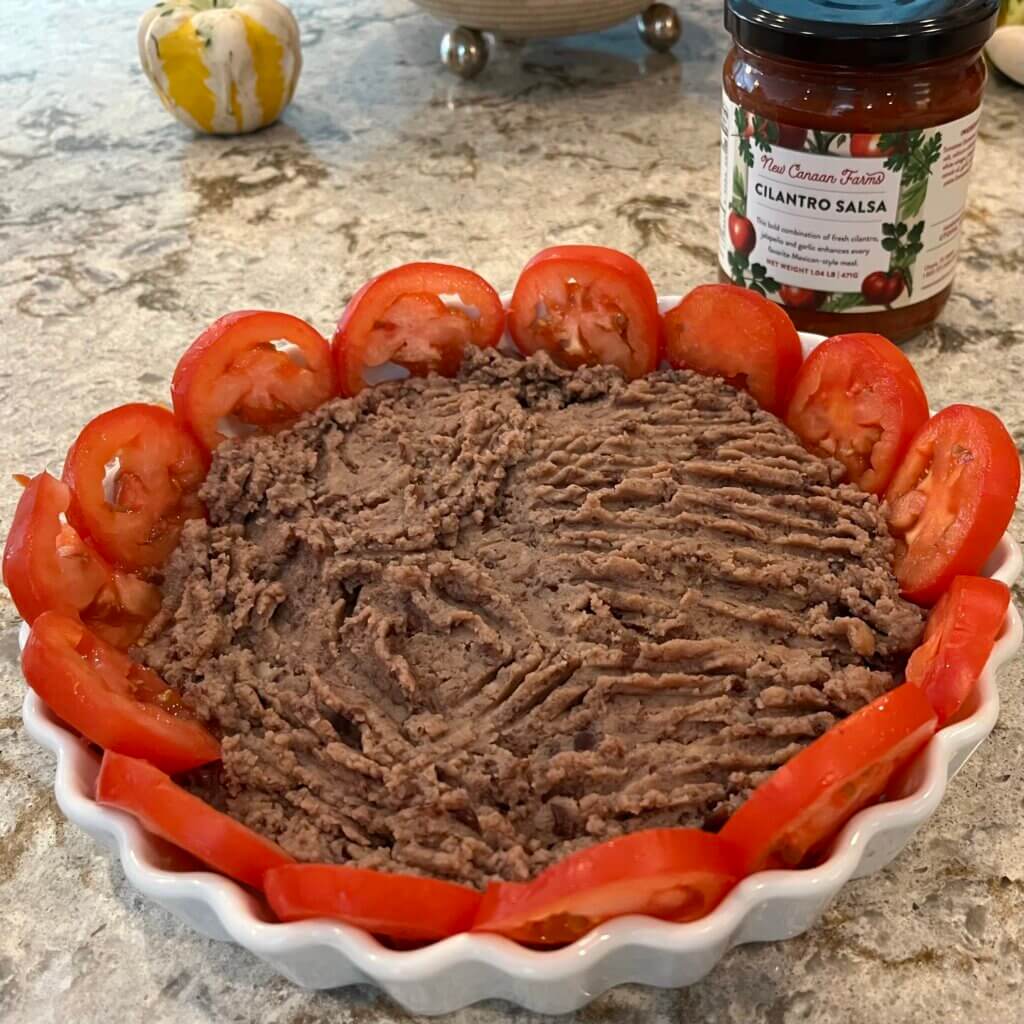 A white pie dish with tomatoes around the edge, and refried beans in the center