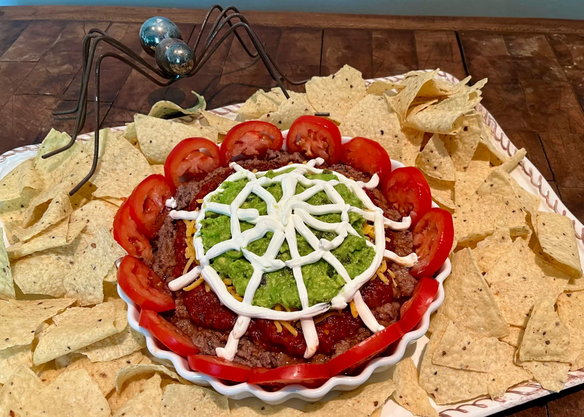 A dish of spooky 5-layer dip, surrounded by tortilla chips and a decorative spider