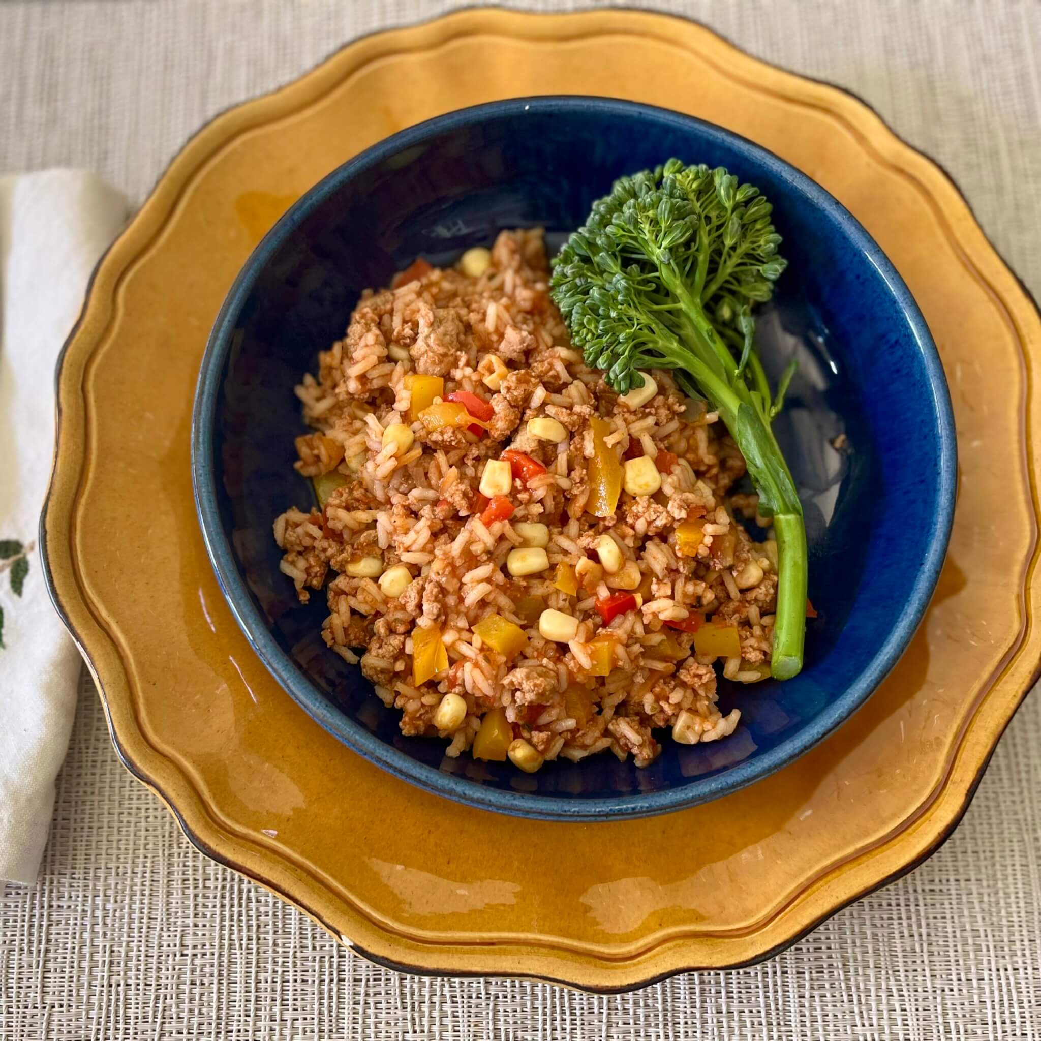 A blue bowl containing a mixture of ground turkey, peppers, corn and salsa, resting on an orange plate