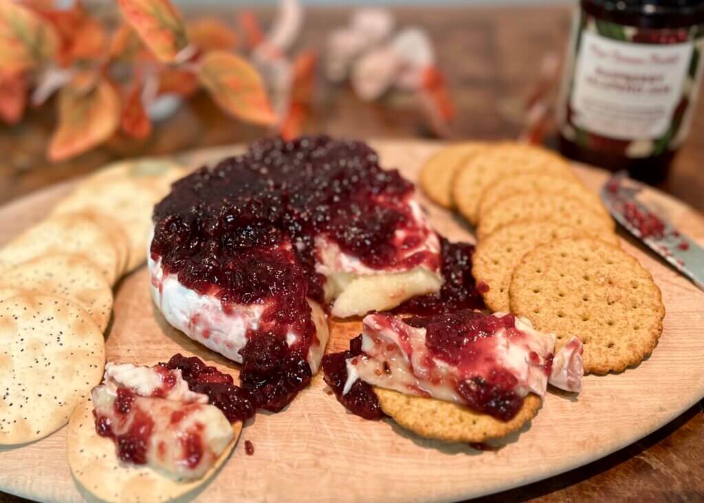 A platter of baked brie and New Canaan Farms Raspberry Jalapeño Jam, surrounded by crackers