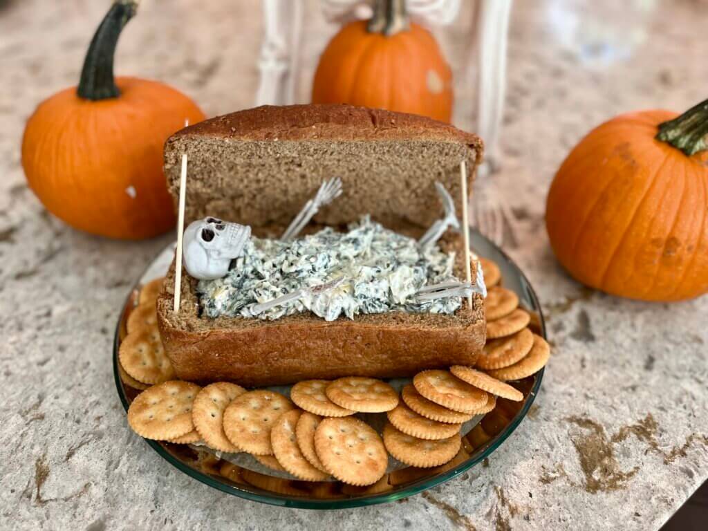 A hollow loaf of wheat bread, made to look like a coffin, containing spooky spinach dip for Halloween