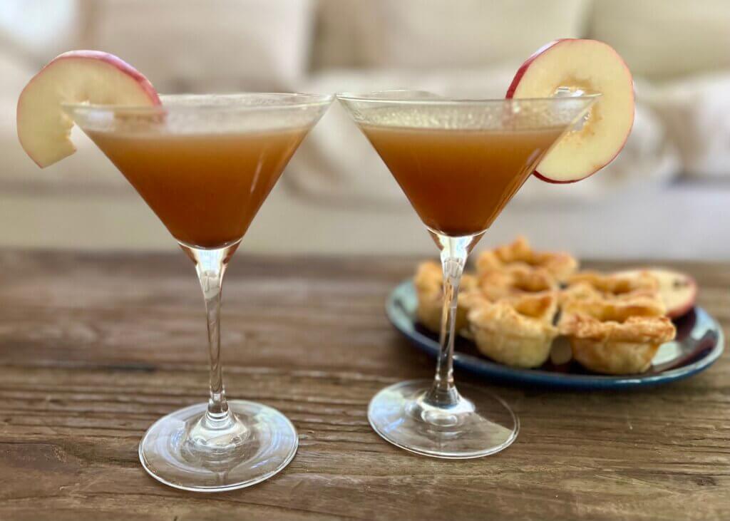 Two martini glasses containing warm apple buttered rum, with a plate of cranberry brie canapés